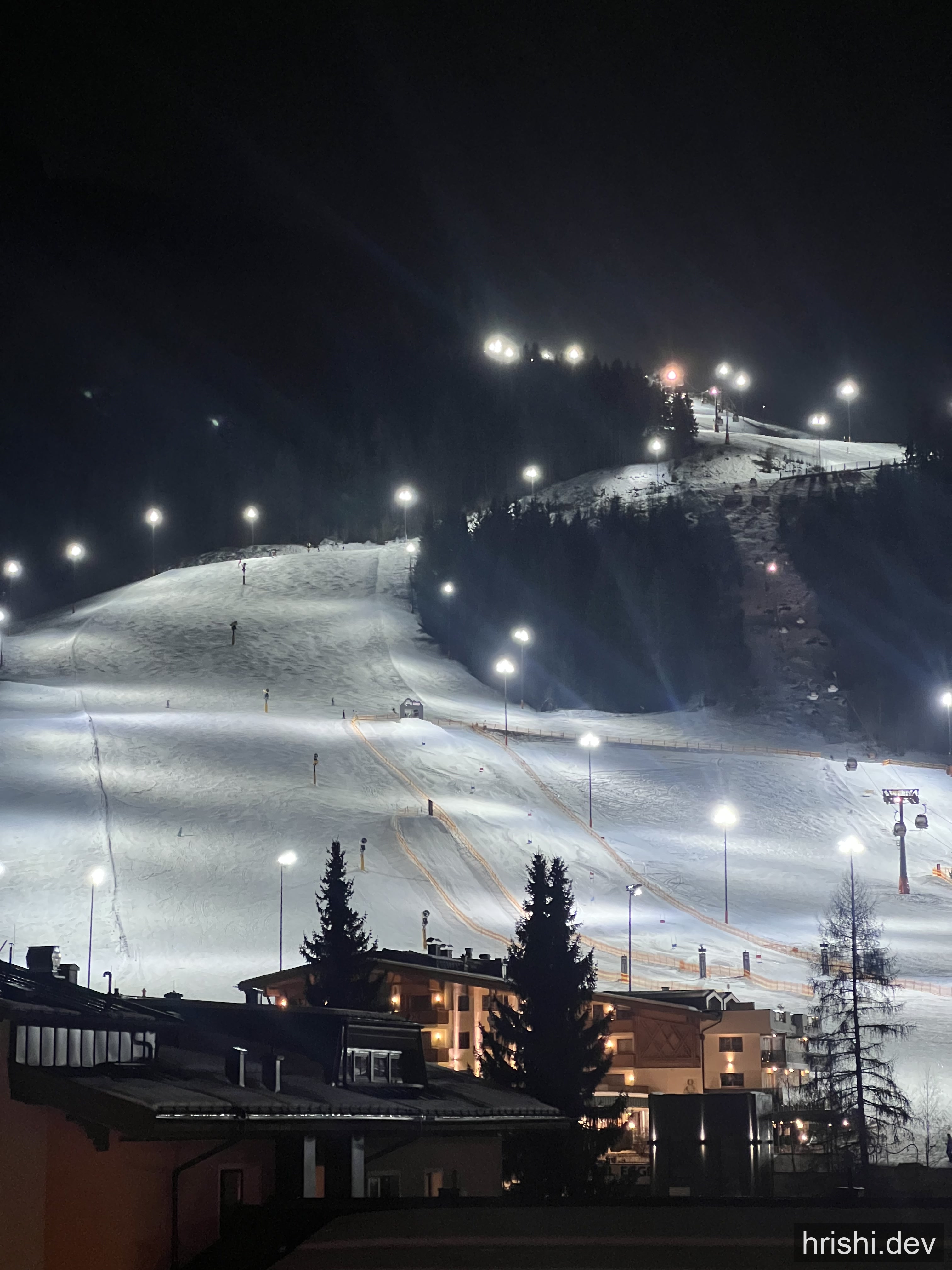 A floodlit ski piste at night in Saalbach, Austria, lined with lights and surrounded by dark mountains