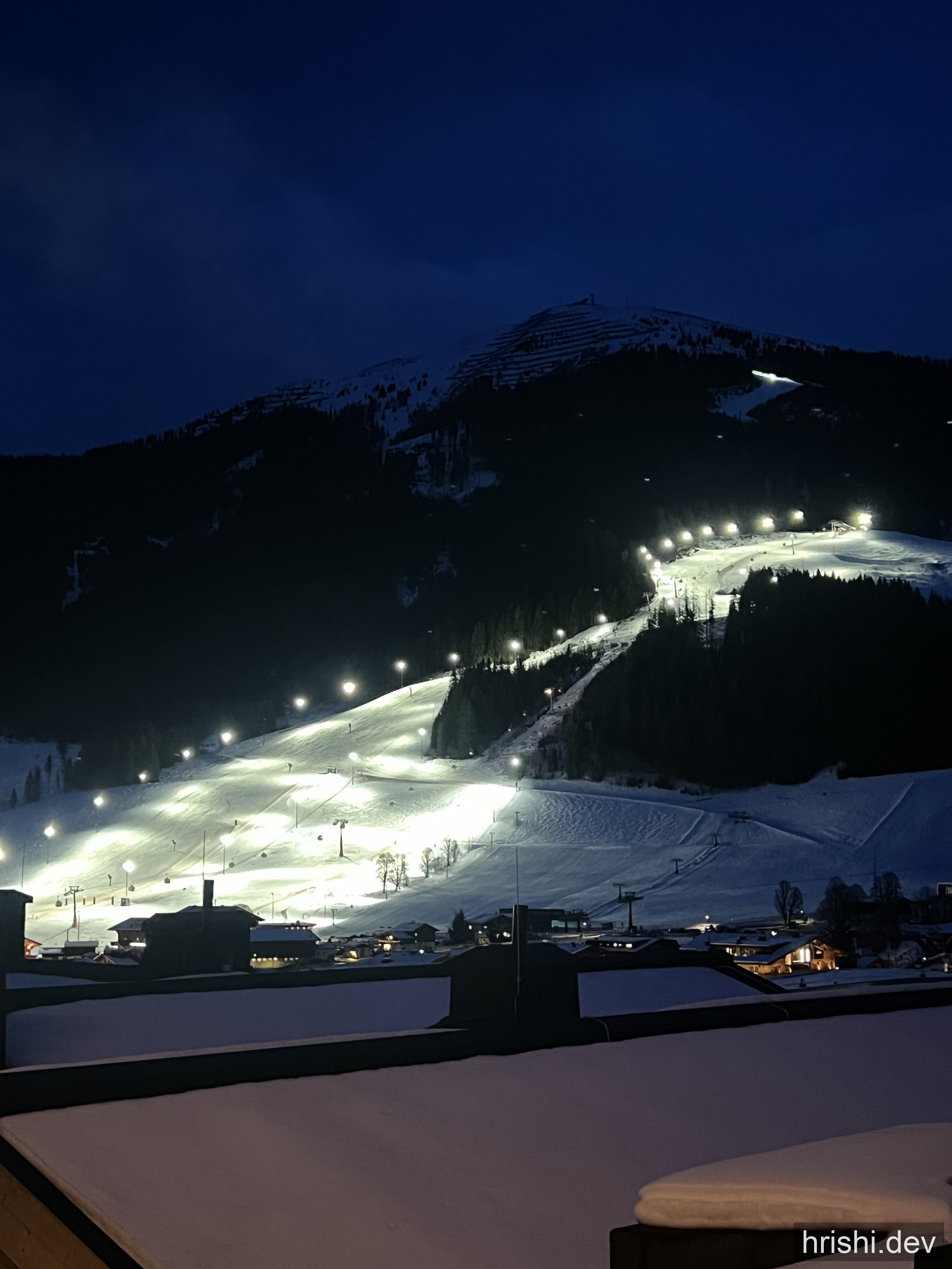 A wide floodlit ski slope at dusk in Saalbach, Austria, with the village lights below